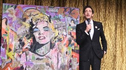 A man in a tuxedo beside a painting of Marilyn Monroe collaged with various materials.